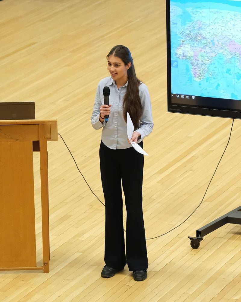 Woman giving a presentation in a lecture hall, holding a microphone with a map displayed on a large screen behind her